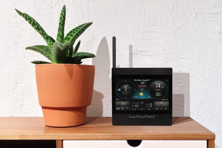 Potted plant beside digital weather station on wooden shelf.